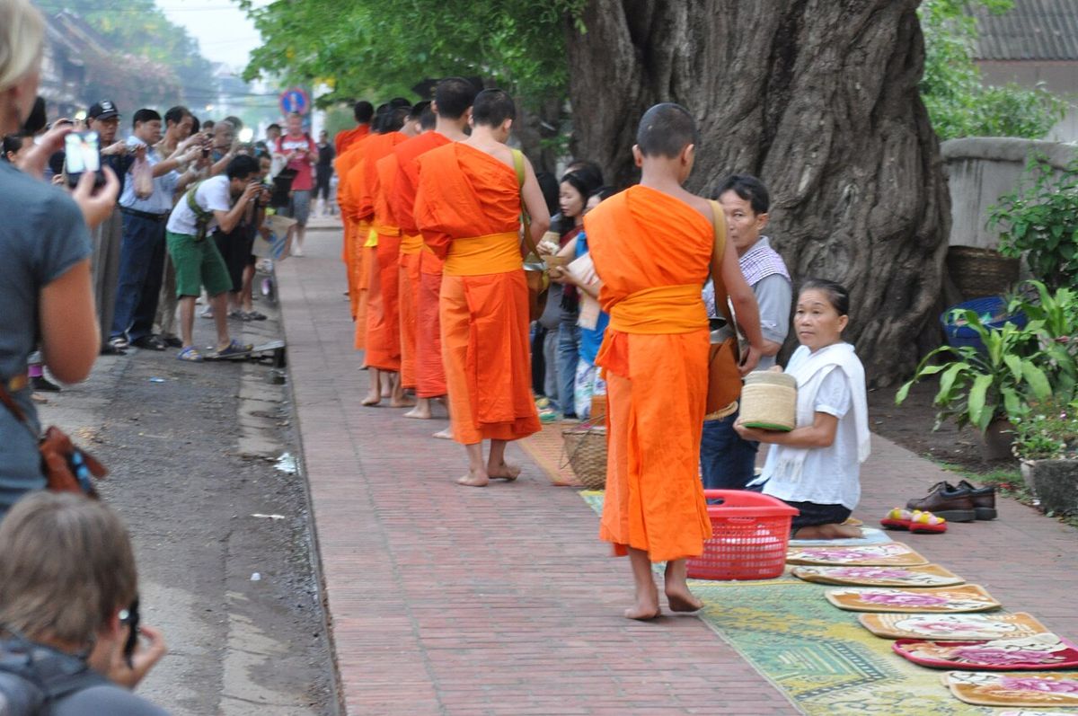 A woman offers food to a young Buddhist monk during the morning alms round