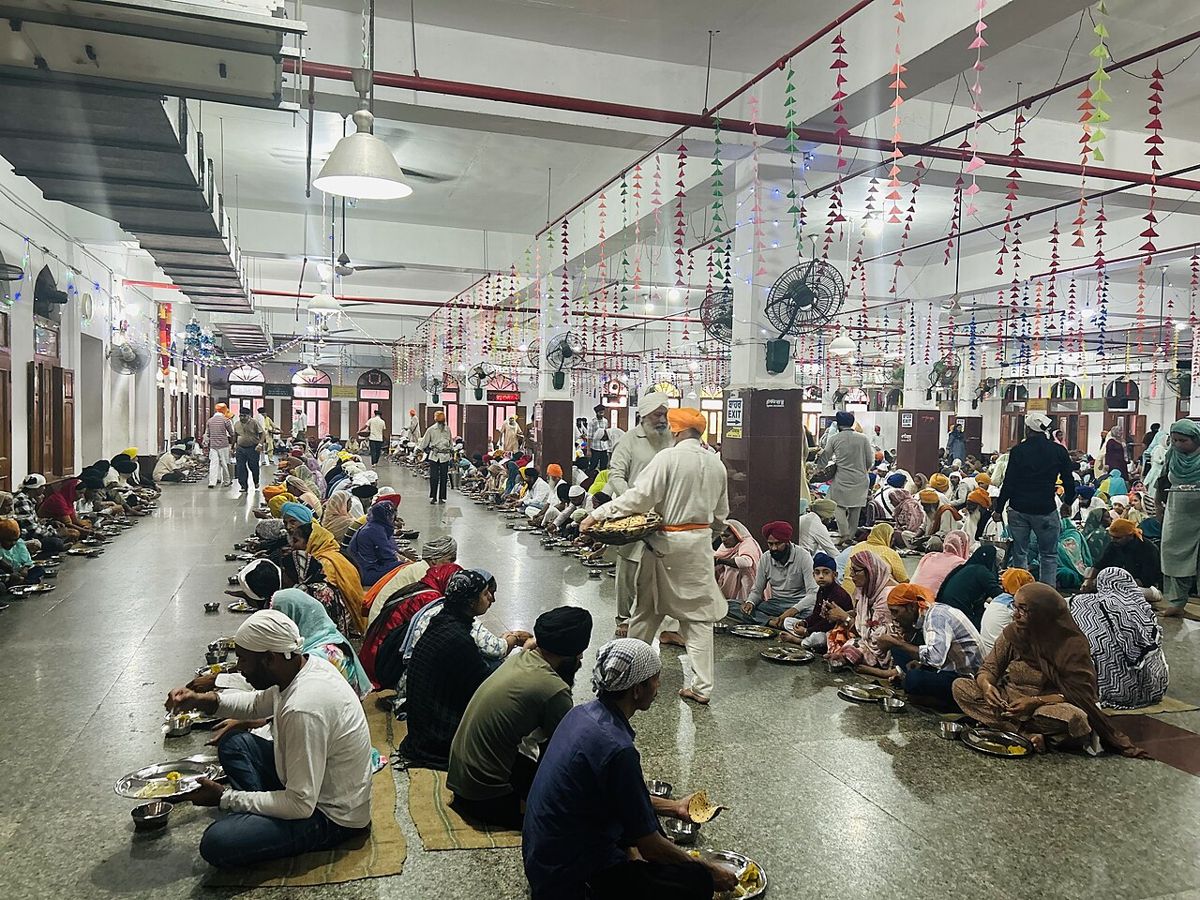 People seated in rows for a free shared meal in the langar hall at the Golden Temple, Amritsar