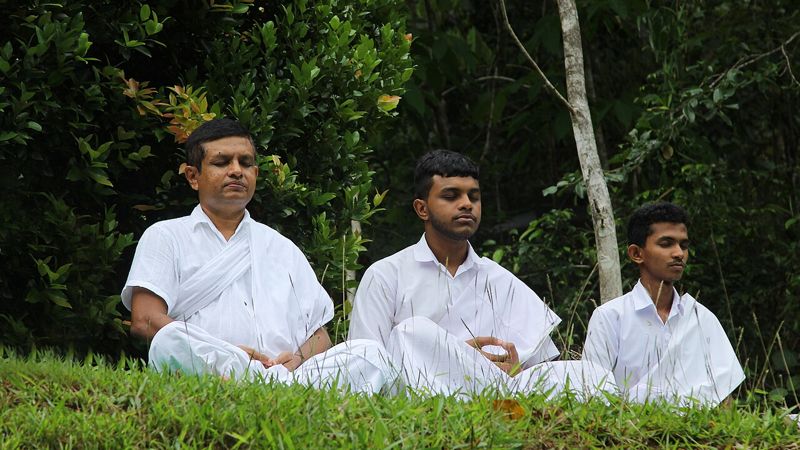 Three men meditating seated on grass