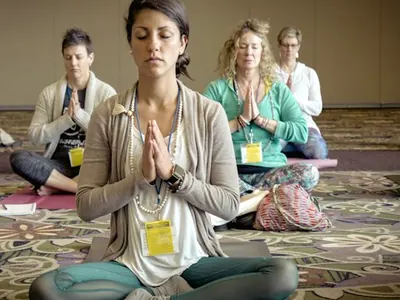 Group of yoga trainees with name badges meditating, hands at heart, in a training room